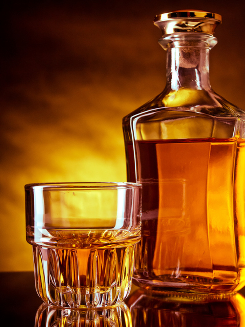 <p>Glass and a bottle of whisky against red and yellow background</p>