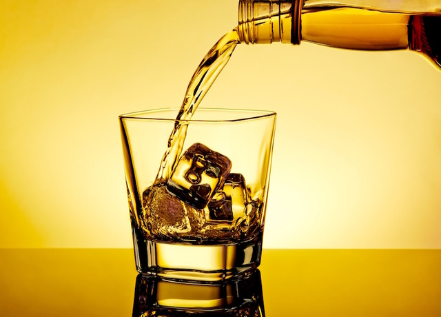 barman pouring whiskey in the glass on table with reflection, warm tint atmosphere